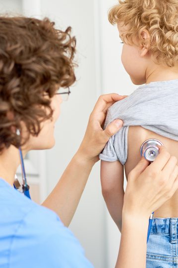 Portrait of female doctor listening to childs breathing from the back using stethoscope to check for symptoms of bronchitis or pneumonia